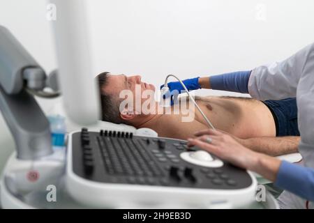 Arzt, der eine doppler-Sonographie bei einem männlichen Patienten in einer Kardiologieklinik macht. Kardiologe, der eine Ultraschalluntersuchung am Herz-Kreislauf-System durchführt Stockfoto