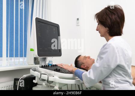 Arzt, der eine doppler-Sonographie bei einem männlichen Patienten in einer Kardiologieklinik macht. Kardiologe, der eine Ultraschalluntersuchung am Herz-Kreislauf-System durchführt Stockfoto