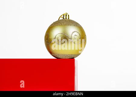 Minimale Weihnachtskomposition. Rotes würfelförmiges Podium mit gelbem Weihnachtsbaum-Spielzeugball auf weißem Hintergrund mit Kopierraum. Stockfoto