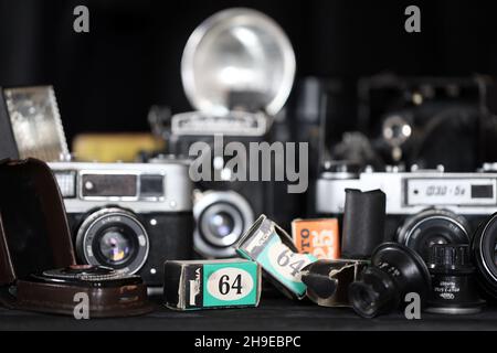 CHARKOV, UKRAINE - 27. APRIL 2021: Filmkameras und eine andere alte Retro-Fotoausrüstung auf schwarzem Holztisch in der Dunkelkammer des Fotografen. Foto Stockfoto