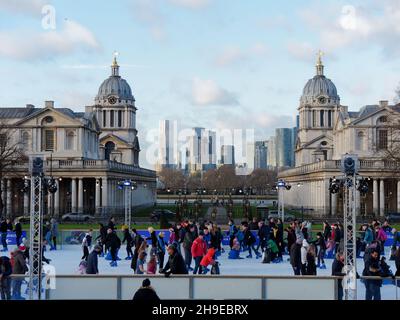 London, Greater London, England, Dezember 04 2021: Menschen laufen auf der Eisbahn in Greenwich zur Weihnachtszeit mit den Universitätsgebäuden hinter sich Stockfoto