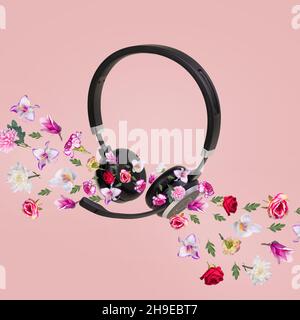 Kreative Komposition aus Kopfhörern und verschiedenen Arten von bunten Blumen, die aus den Kopfhörern herauskommen, isoliert auf einem leuchtend rosa Hintergrund. Stockfoto