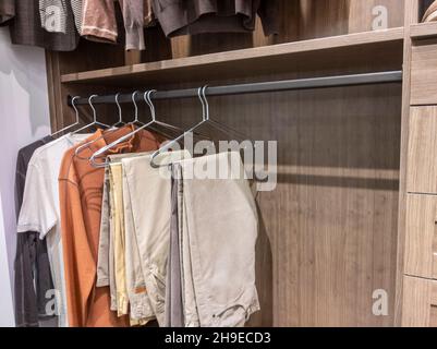 Ein großer begehbarer Schrank mit Hemden und Khaki-Hosen, die an Kleiderbügeln hängen Stockfoto