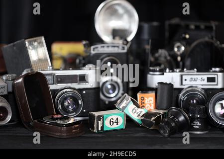 CHARKOV, UKRAINE - 27. APRIL 2021: Filmkameras und eine andere alte Retro-Fotoausrüstung auf schwarzem Holztisch in der Dunkelkammer des Fotografen. Foto Stockfoto