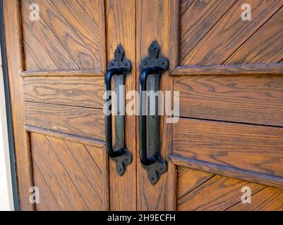 Schräg Blick auf rustikale Holztüren mit schwarzen Eisengriffen auf ein helles Gebäude Stockfoto