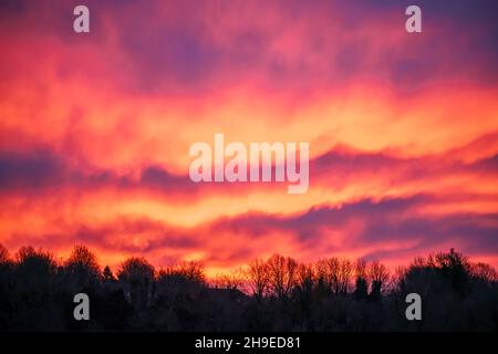 Wunderschöne Wellen von feuriger Lava wie Wolke in einem leuchtend roten, orangefarbenen und gelben Sonnenaufgangshimmel, Wiltshire UK Stockfoto