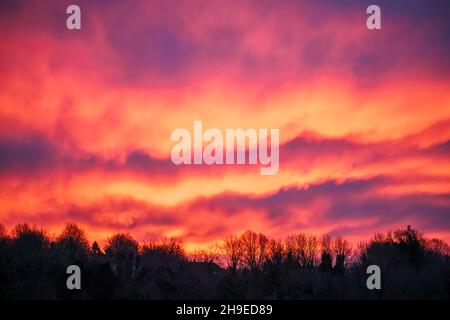 Wunderschöne Wellen von feuriger Lava wie Wolke in einem leuchtend roten, orangefarbenen und gelben Sonnenaufgangshimmel, Wiltshire UK Stockfoto