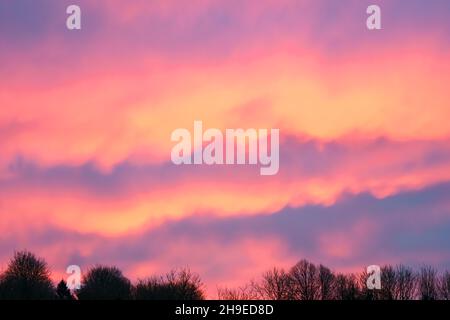 Wunderschöne Wellen von feuriger Lava wie Wolke in einem leuchtend roten, orangefarbenen und gelben Sonnenaufgangshimmel, Wiltshire UK Stockfoto