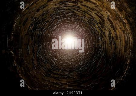 Im Inneren des alten Ziegelrohrschachts mit Leiter. Stockfoto