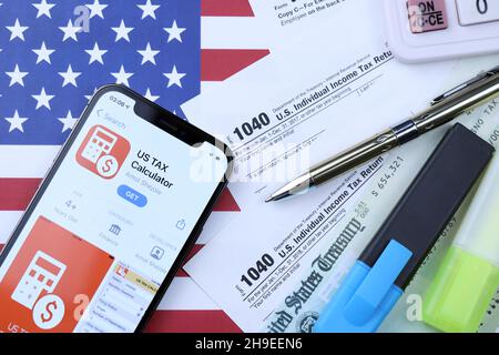 CHARKOW, UKRAINE - 5. MÄRZ 2021: US-Steuerrechner-App auf dem iPhone 12 Pro-Bildschirm mit 1040 und w-2 Papiersteuerformularen auf US-Flagge Stockfoto