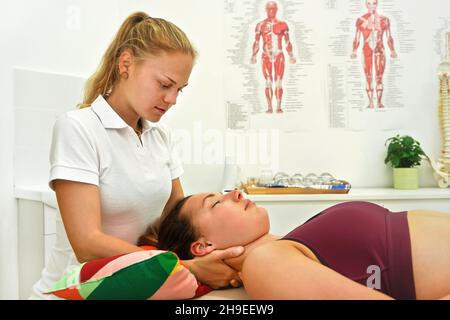 Physiotherapeutin massiert Muskeln am Hals ihres Klienten, der am Tisch liegt Stockfoto