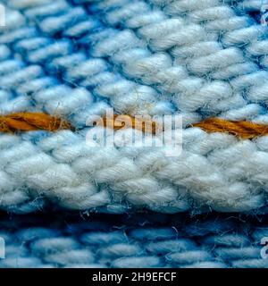 Makro-Closeup Denim-Jeans-Naht-Struktur am Saum in Orange und Blau Stockfoto