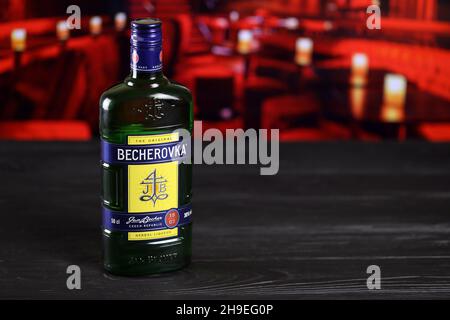 CHARKOW, UKRAINE - 14. FEBRUAR 2021: Kräuterlikör-Flasche Becherovka auf Holztisch mit roter Bar im Hintergrund. Elite-Alkoholproduktion Stockfoto