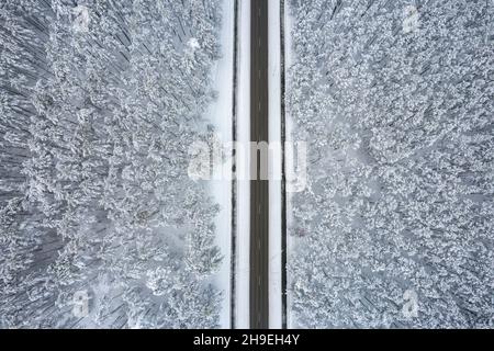 Luftaufnahme der Asphaltstraße, die durch frostige Winterwälder und mit Reif und Schnee bedeckte Haine führt. Drohnenfoto von schwarzer Straßenlinie und Bäumen mit kühlem Schnee in den Bergen. Weihnachtsthema Stockfoto