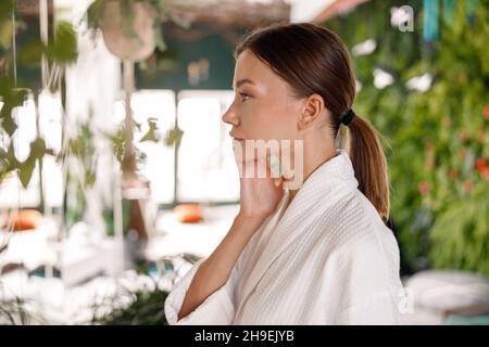 Seitenansicht Porträt einer hübschen jungen Frau im Bademantel, die Schönheitsbehandlungen genießt und sich um ihre Haut kümmert Stockfoto