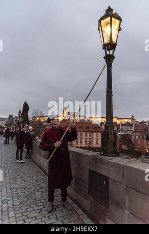 Prag, Tschechische Republik. 06th Dez 2021. Ein Feuerzeug mit einer traditionellen Uniform in Rot und Schwarz leuchtet eine Gaslampe auf der berühmten Karlsbrücke im Zentrum von Prag. Während der Adventszeit werden Gaslampen von lamplighter anstelle einer automatisierten Anlage, die das restliche Jahr über im Einsatz ist, beleuchtet. Die Straßenbeleuchtung in Prag geht auf das Jahr 1847 zurück. Gaslampen wurden bis 1985 verwendet. Im Jahr 2002 wurden Gaslampen im Stadtzentrum wieder eingeführt. Kredit: SOPA Images Limited/Alamy Live Nachrichten Stockfoto