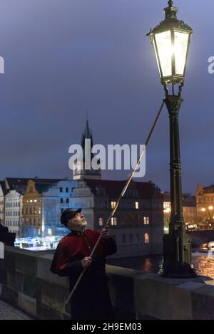 Prag, Tschechische Republik. 06th Dez 2021. Ein Feuerzeug mit einer traditionellen Uniform in Rot und Schwarz leuchtet eine Gaslampe auf der berühmten Karlsbrücke im Zentrum von Prag. Während der Adventszeit werden Gaslampen von lamplighter anstelle einer automatisierten Anlage, die das restliche Jahr über im Einsatz ist, beleuchtet. Die Straßenbeleuchtung in Prag geht auf das Jahr 1847 zurück. Gaslampen wurden bis 1985 verwendet. Im Jahr 2002 wurden Gaslampen im Stadtzentrum wieder eingeführt. (Foto von Tomas Tkacik/SOPA Images/Sipa USA) Quelle: SIPA USA/Alamy Live News Stockfoto