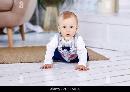 Auf allen Vieren kriecht ein Kleinkind über den bemalten Dielenboden des Wohnzimmers. Stockfoto