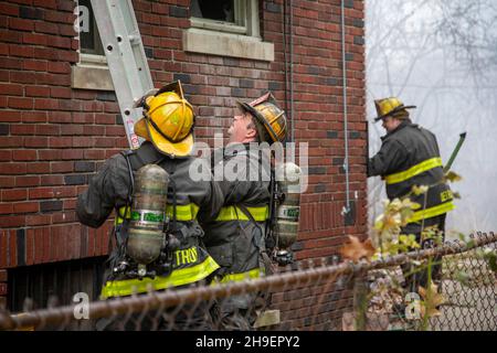 Detroit, Michigan - die Feuerwehrleute, die Lufttanks trugen, stellten eine Leiter auf, während sie ein Feuer bekämpfen, das ein Haus in Detroits Morningside-Nachbarschaft beschädigt hat. Stockfoto