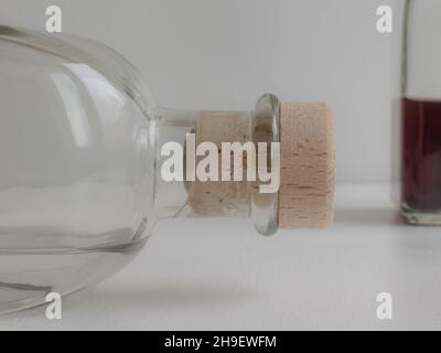 Nahaufnahme aus Glasflasche mit Kork auf verschwommenem weißem Hintergrund und natürlichem Licht auf dem Tisch Stockfoto