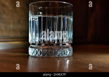 Scharfe Kanten eines Glases schließen sich bei dunkler Beleuchtung auf den Tisch Stockfoto