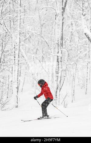 Alpinski. Frau Skifahrerin geht waghhill schnell vor schneebedeckten Bäumen Hintergrund während Winter Schneesturm. Frau in roter Jacke und Brille. Winter Stockfoto