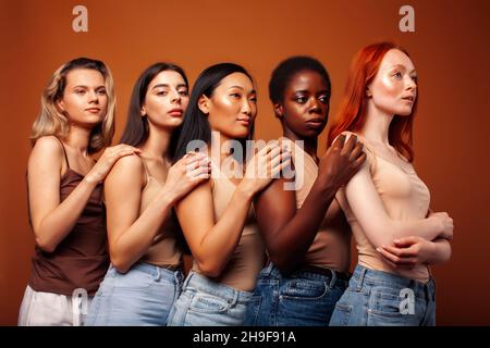 Junge hübsche kaukasische, afro, skandinavische Frau posiert fröhlich zusammen auf braunem Hintergrund, Lifestyle diverse Nationalität Menschen Konzept Stockfoto