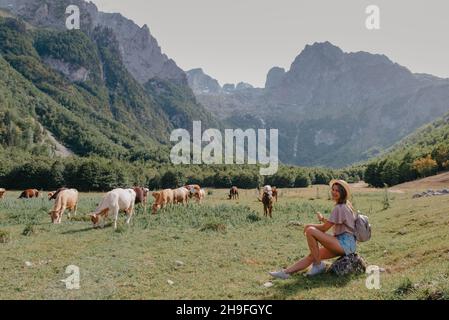 Reise-, Lifestyle-Konzept. Schöne Frau genießt Aussicht auf das Alpendorf in den Alpen. Junge Frau sitzt und entspannt auf dem Berg Stockfoto