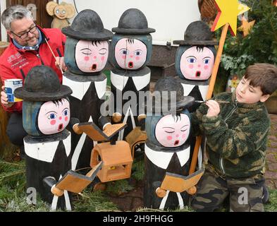 05. Dezember 2021, Sachsen, Borsdorf: Denny Pfaff (l.) und sein Sohn Felix reparieren die abgebropfte Farbe der Liedgesänger, die den Vorgarten der Pfaff-Familien mit neuer Farbe auf Wasserbasis schmücken. Die bis zu 1,20 Meter hohen Sänger wurden vor über 10 Jahren von Förster Manfred Pfaff mit einer Kettensäge aus Weimut-Kiefer gefertigt. Sie begeistern die Menschen der sächsischen Gemeinde Wermsdorf und vorbeifahrende Autofahrer jedes Jahr bis zum 6. Januar. Die Holzkaroliere gehören zu etwa 50 handgesägten Figuren, Pilzen, Blumenbänken und Sitzanordnungen, die der Hobby-Kettensägenkünstler gemacht hat. Foto: Stockfoto