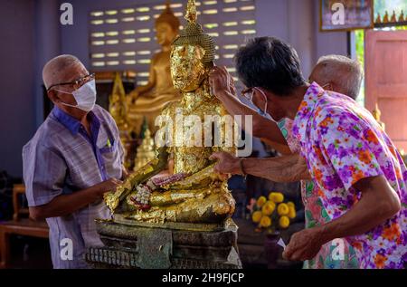 Männer legen während der Songkran-Feierlichkeiten im ländlichen Thailand Goldfolie auf eine Statue des Buddha. Stockfoto