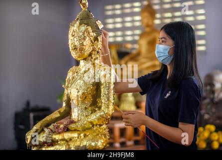 Eine Frau legt während der Songkran-Feierlichkeiten Goldfolie in eine Buddha-Statue. Stockfoto