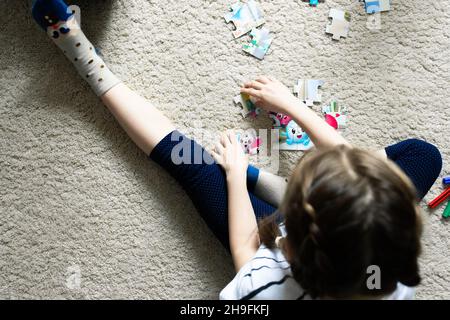 Ein Mädchen spielt in ihrem Zimmer, sammelt ein Puzzle. Blick von oben. Stockfoto