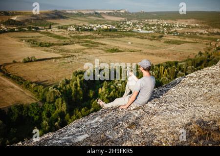 Rückansicht eines jungen Mannes, der Tee oder Kaffee in den Bergen trinkt. Reisender Mann mit Bart hält in den Händen eine Tasse Tee, nach dem Wandern. Reisen, Lifestyle, Urlaub. Stockfoto