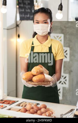 Porträt des glücklichen jungen Street Food Cart Besitzer in medizinische Maske hält Tablett mit Sandwiches Stockfoto