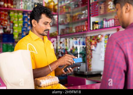 Indischer Kunde, der mit Kreditkarte im Lebensmittelgeschäft oder im Kirana-Shop bezahlt - Konzept der digitalen oder bargeldlosen Zahlung, Finanzen und Kleinunternehmen. Stockfoto