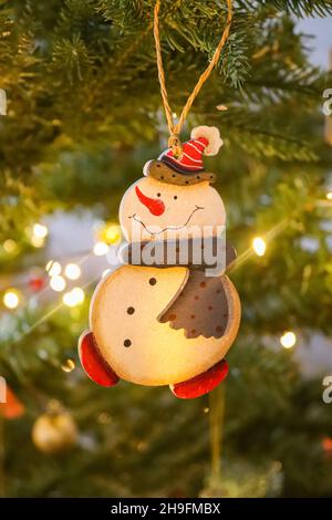 Hölzerner Schneemann als Weihnachtsbaumschmuck, der an einem künstlichen Weihnachtsbaum hängt Stockfoto