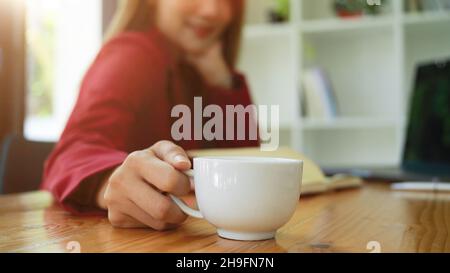 Nahaufnahme einer Geschäftsfrau oder Managerin, die eine Kaffeetasse an ihrem Schreibtisch im Büro hält. Stockfoto