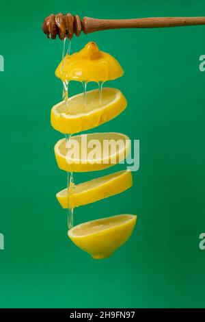 Zitronenscheiben schweben auf grünem Hintergrund mit Honigtropfen Stockfoto