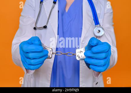 Eine Krankenschwester auf rotem Hintergrund zeigt Hände in Handschellen, Nahaufnahme. Arzt wegen einer Bestechung von einem Patienten verhaftet, Konzept Stockfoto