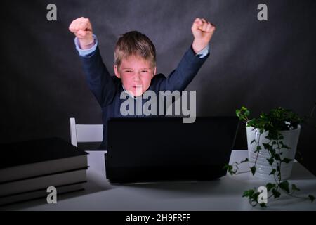 Der Junge hebt seine Hände in einer siegreichen Geste, kopiert Raum auf einen dunklen Studiohintergrund Stockfoto