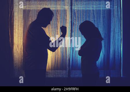 Silhouette eines streitsüchtige Mannes und einer Frau am Nachtfenster. Verheiratetes Paar Ehemann und Ehefrau, Gewalt im Abendlicht des Wohnzimmers Stockfoto