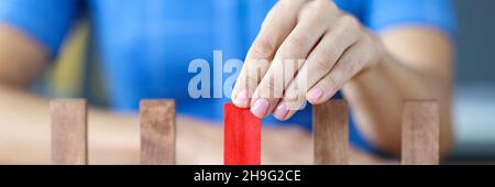 Die Frau wählt einen roten Holzblock aus vielen beigen Holzblöcken in Reihe Stockfoto