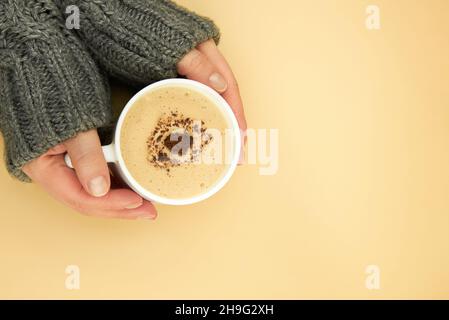 Die Hände einer Frau in einem warmen Pullover halten eine Tasse Kaffee. Stockfoto