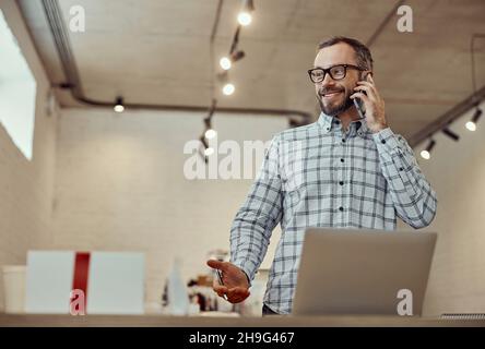 Fröhlicher Mann, der im Café mit dem Handy sprach und ein Notebook benutzte Stockfoto