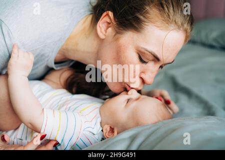 Nahaufnahme fürsorgliche junge Mutter küsst ihr neugeborenes Baby. Sanfte Erziehung, Umarmungen und Streicheleinheiten. Stockfoto