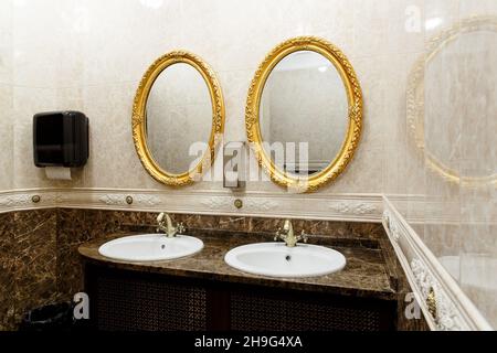 Zwei moderne Keramikwaschbecken mit Spiegeln in der Toilette des Restaurants. Keramikwaschbecken mit Bronze-Mixer in zeitgemäßer Toilette. Innenansicht von Euro Stockfoto
