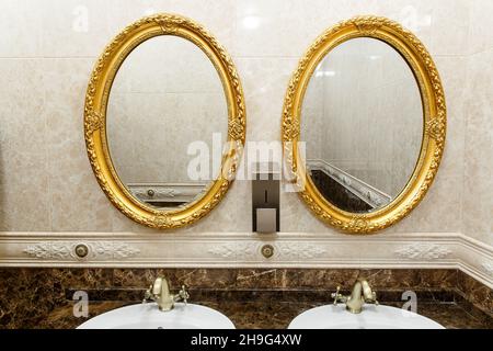 Zwei moderne Keramikwaschbecken mit Spiegeln in der Toilette des Restaurants. Keramikwaschbecken mit Bronze-Mixer in zeitgemäßer Toilette. Innenansicht von Euro Stockfoto