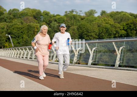 Positives Seniot-Paar mit Wasserflaschen trainiert gemeinsam auf dem Steg Stockfoto