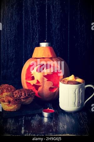 Herbstkomposition mit geschnitztem Kürbis, heißem Kürbis-würzigem Getränk und Muffins Stockfoto