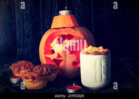 Herbstkomposition mit geschnitztem Kürbis, heißem Kürbis-würzigem Getränk und Muffins Stockfoto
